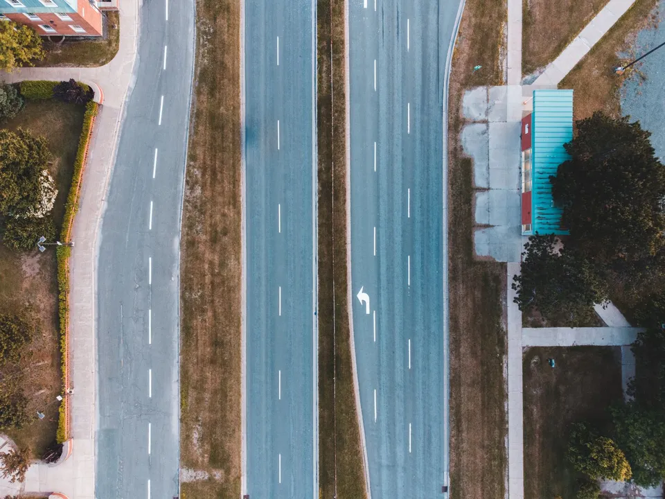 Bird's eye view of an empty urban two-lane highway with adjacent bus stop and greenery.