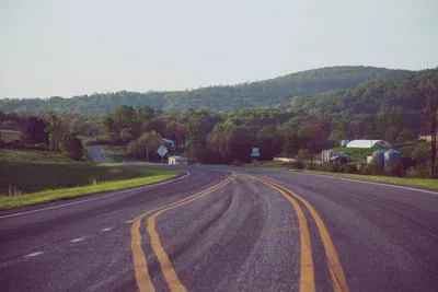 Peaceful country road winding through lush green hills under a clear sky.
